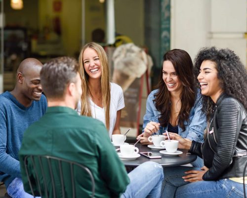 Multiracial group of five friends having a coffee together. Three women and two men at cafe, talking, laughing and enjoying their time. Lifestyle and friendship concepts with real people models