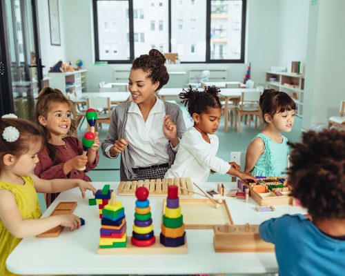 Kids and teacher sitting at the table and playing with toys