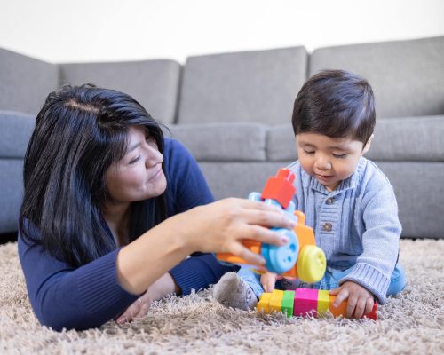 Mexican mother playing with son on carpet at home