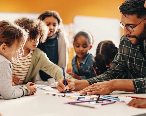 Art and creativity in an elementary school class. Teacher shows his students how to draw using a colouring pencil in a classroom. Primary education and child mentorship.